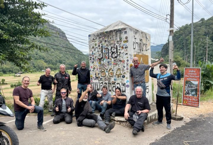 Motorcycle tour group celebrating at a roadside milestone in Northern Thailand