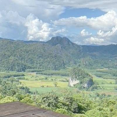 Scenic mountain valley in Northern Thailand with lush green fields and limestone hills under a cloudy sky