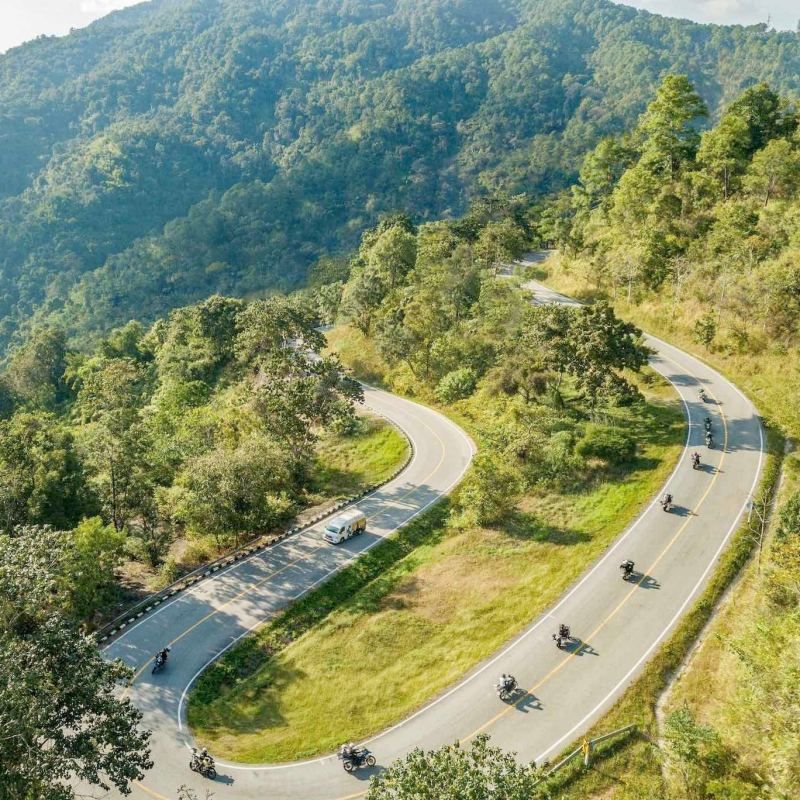 Motorcycle tour group riding along a winding mountain road surrounded by forest in Northern Thailand