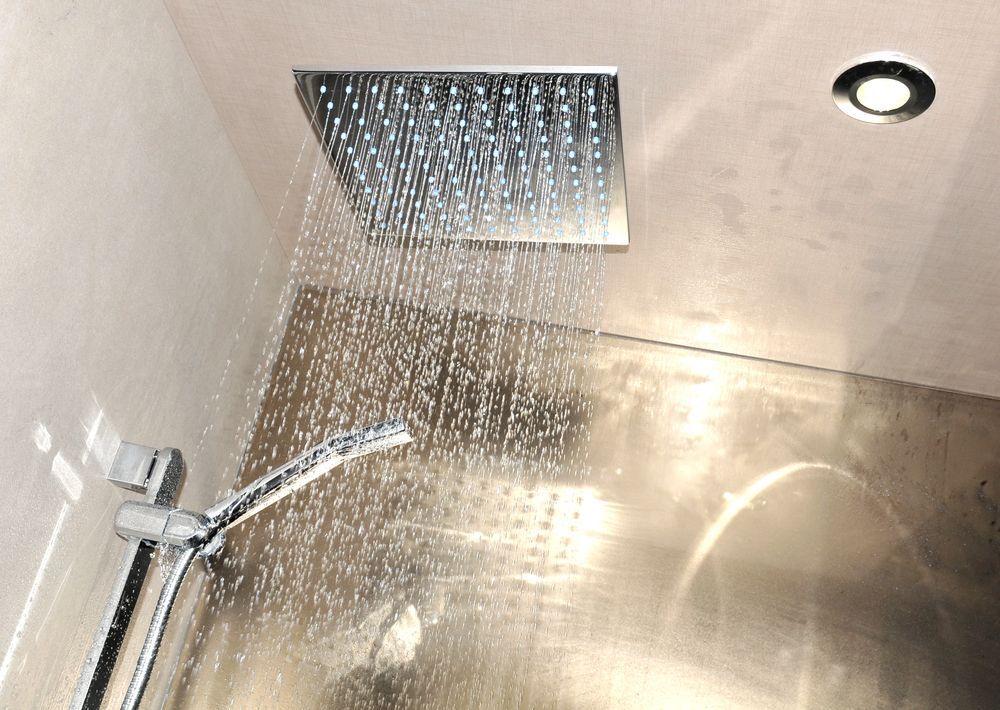 Doccia a soffitto con getto d'acqua sulle pareti in acciaio inox, con soffione e scarico a vista.