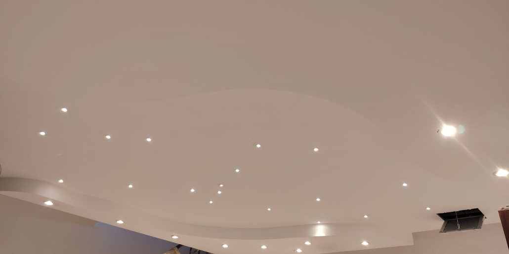 Soffitto con numerose piccole luci a incasso e un lampadario luminoso in una stanza moderna.