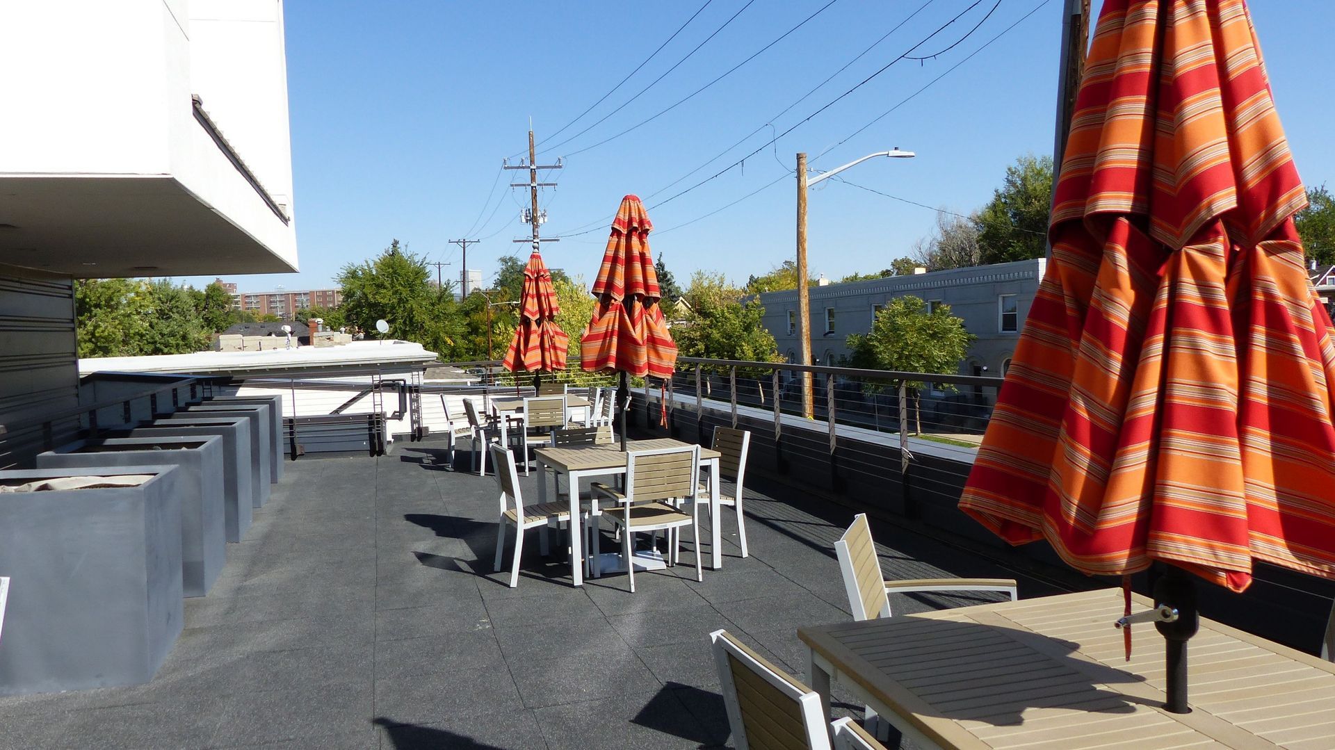 An outdoor rooftop patio with tables and bright orange striped umbrellas on a sunny day.
