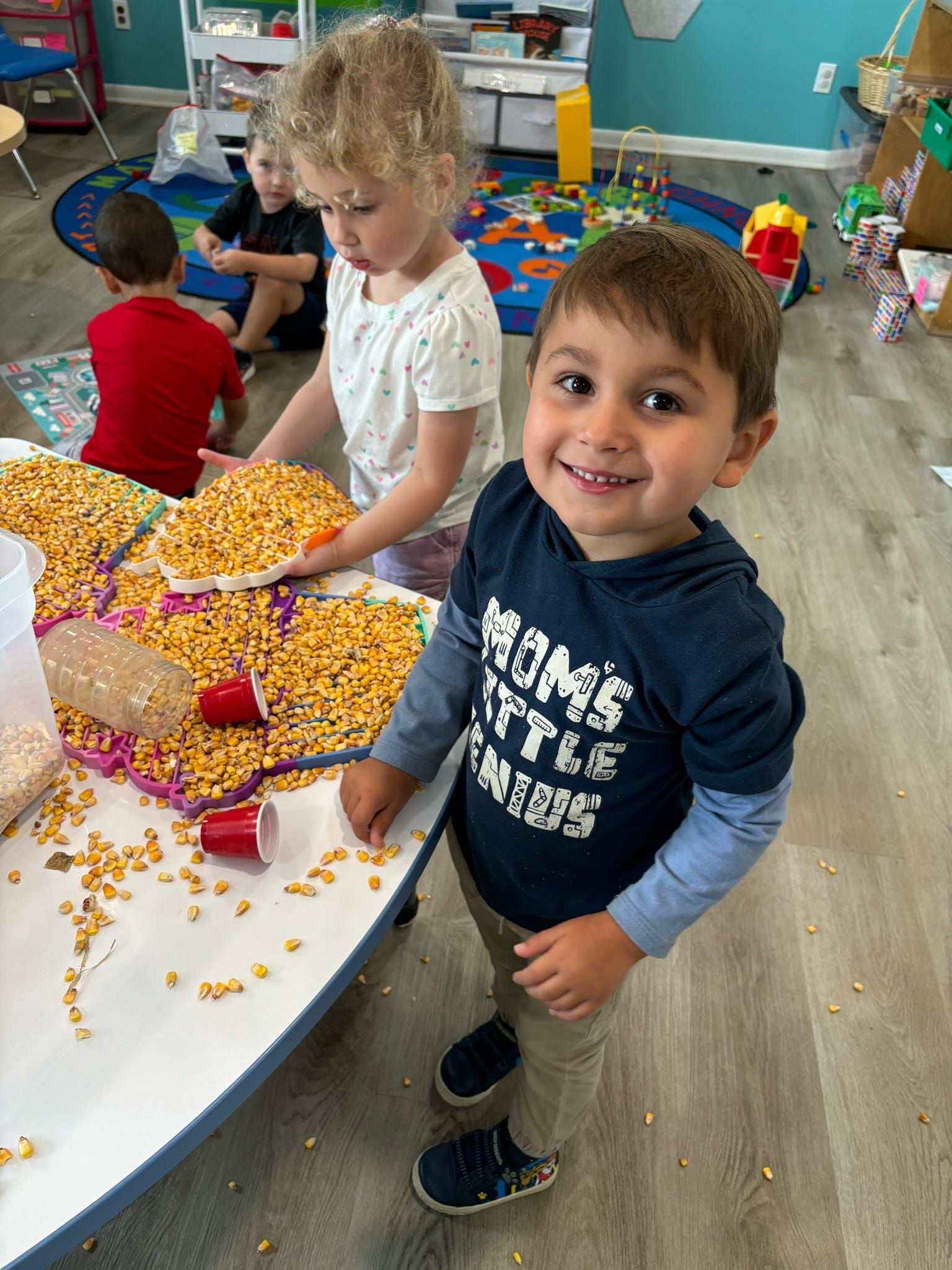 A boy in a blue shirt is standing in front of a table covered in corn.