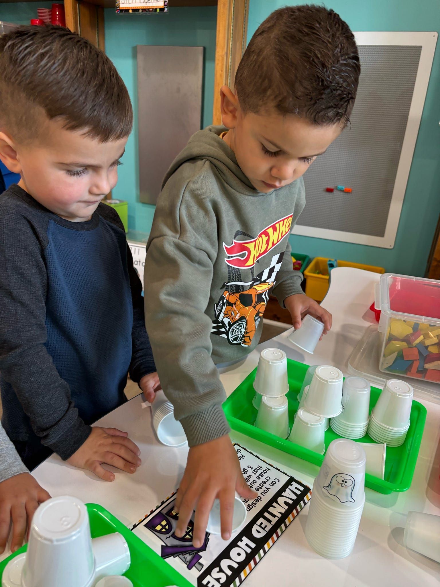 Two young boys are playing with plastic cups on a table.