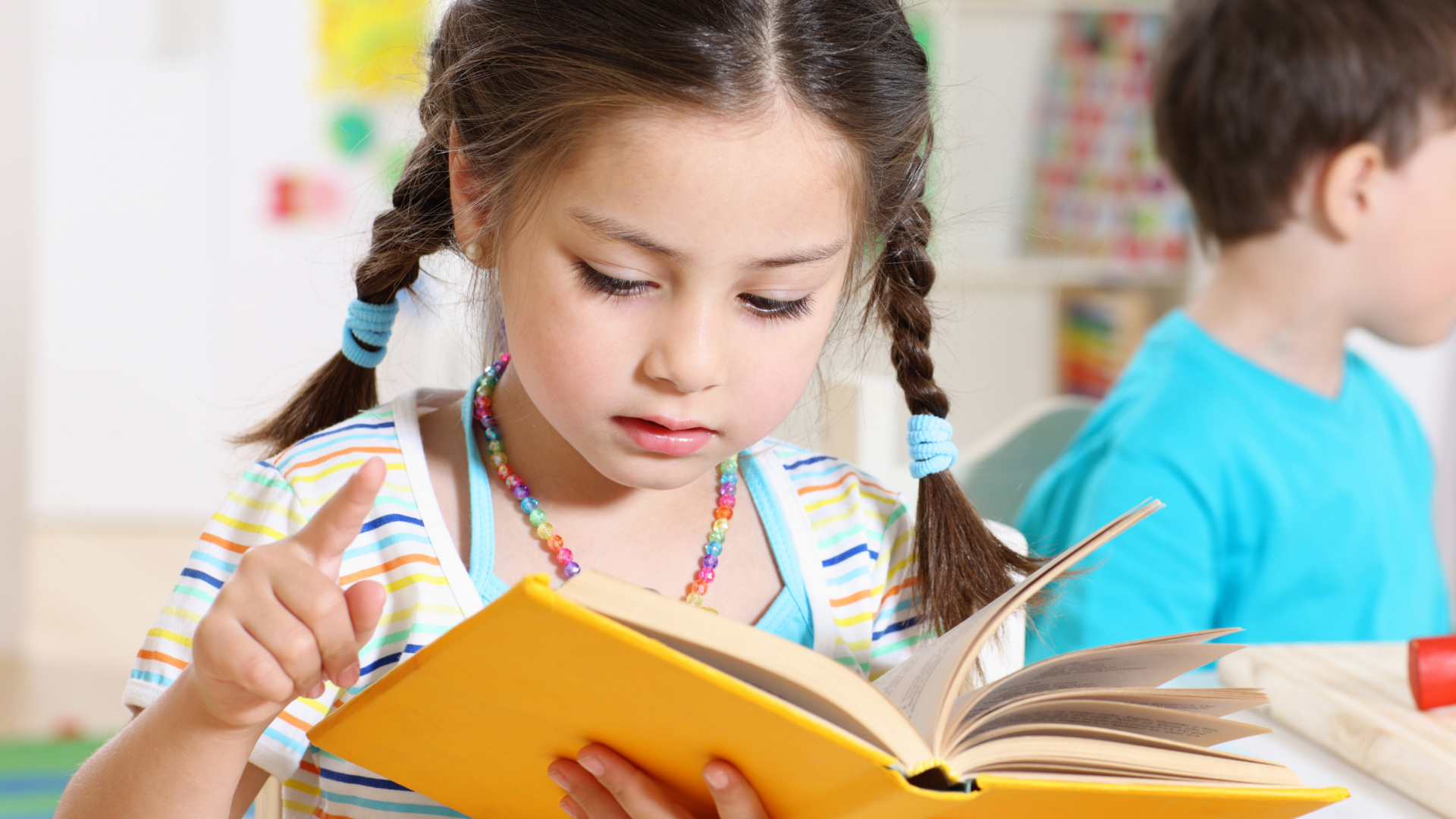 A little girl is reading a book in a classroom.