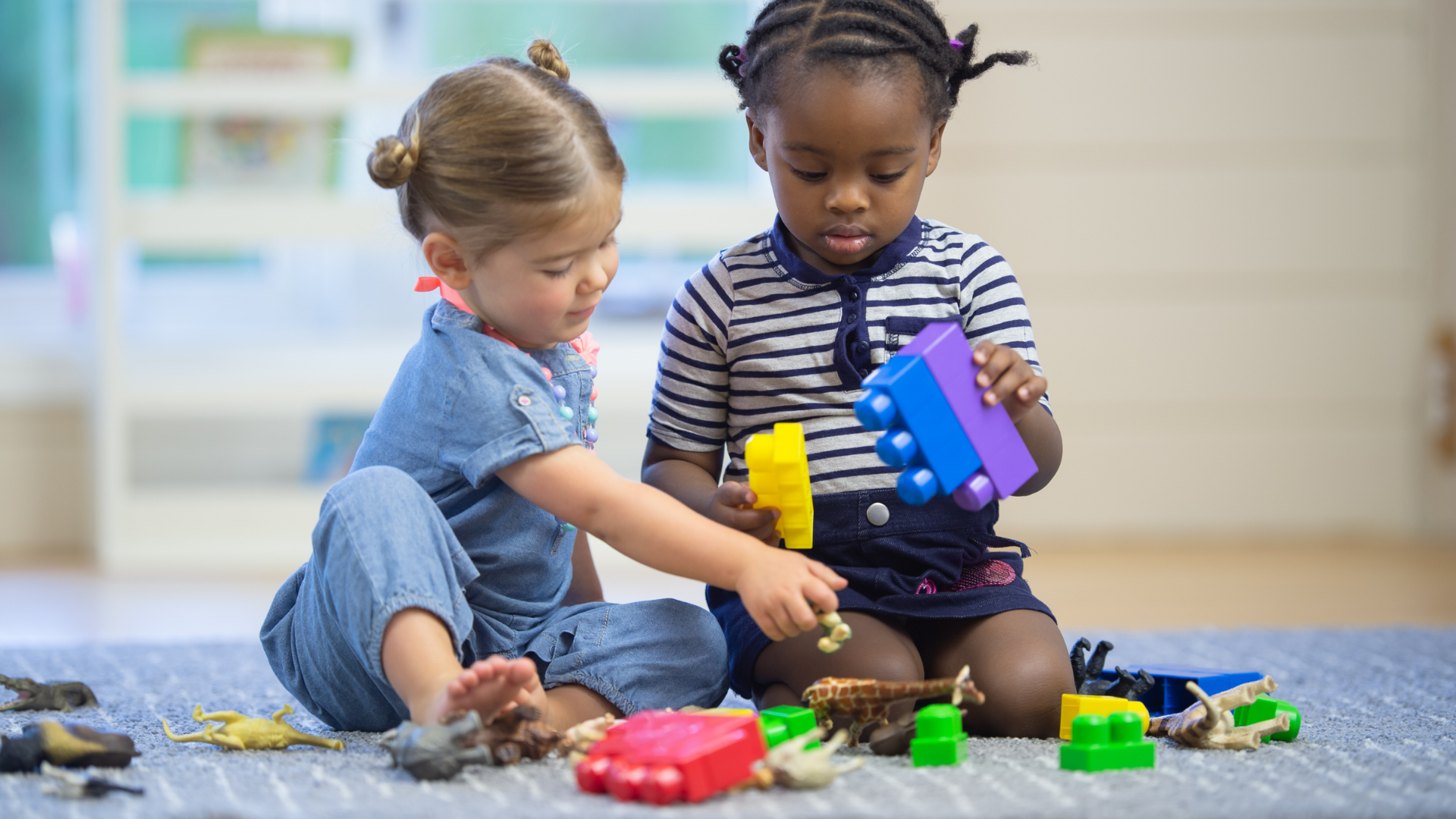 Two little girls are sitting on the floor playing with toys.