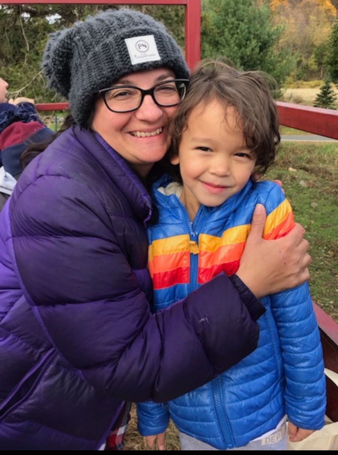 A woman in a purple jacket is hugging a little boy in a blue jacket