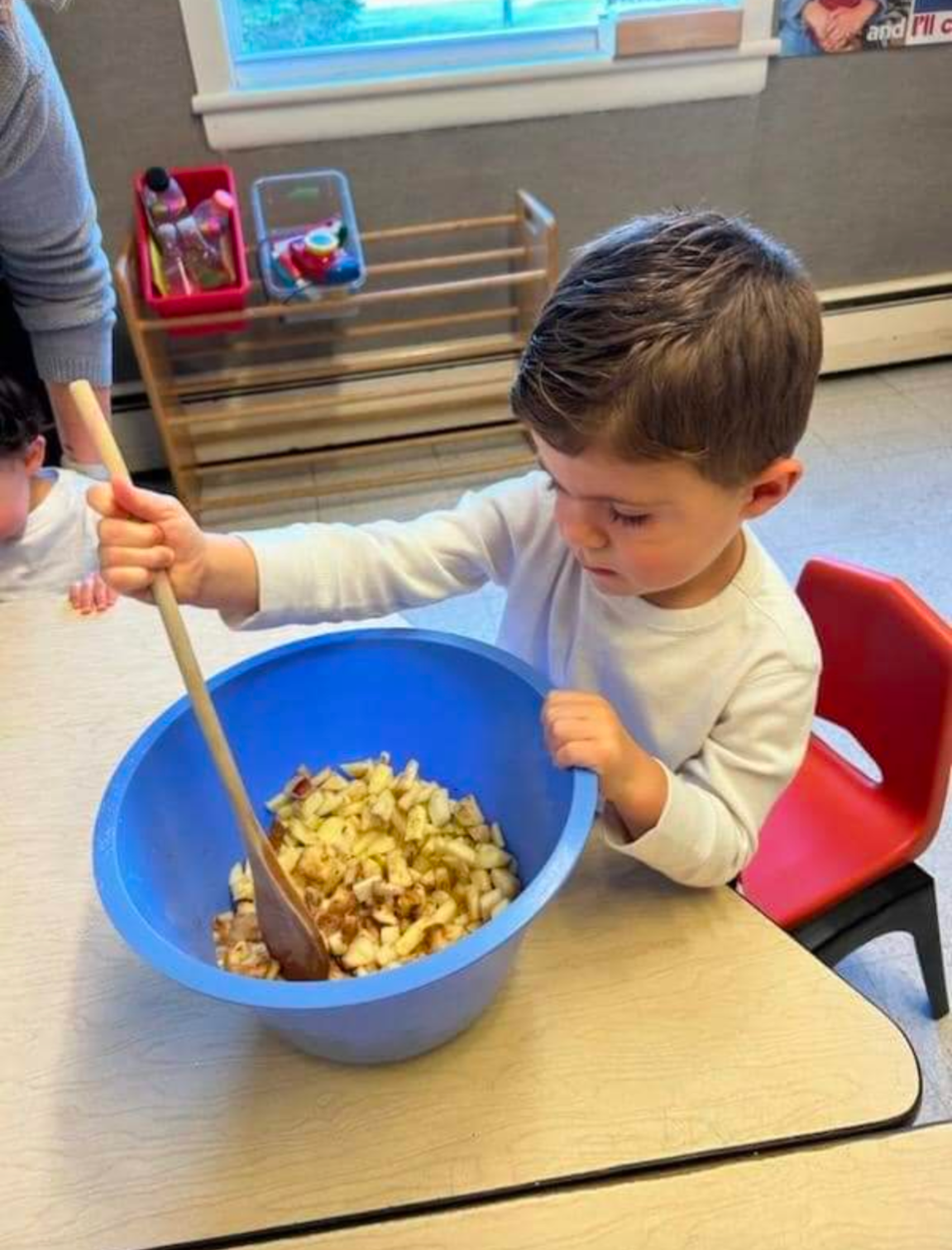 A young boy is stirring a bowl of food with a wooden spoon.