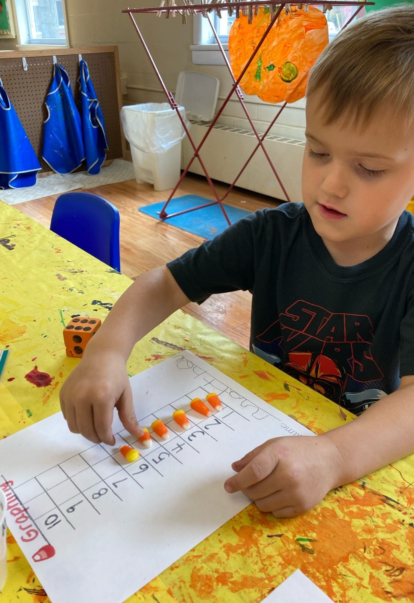 A young boy is sitting at a table playing with corn on the cob.