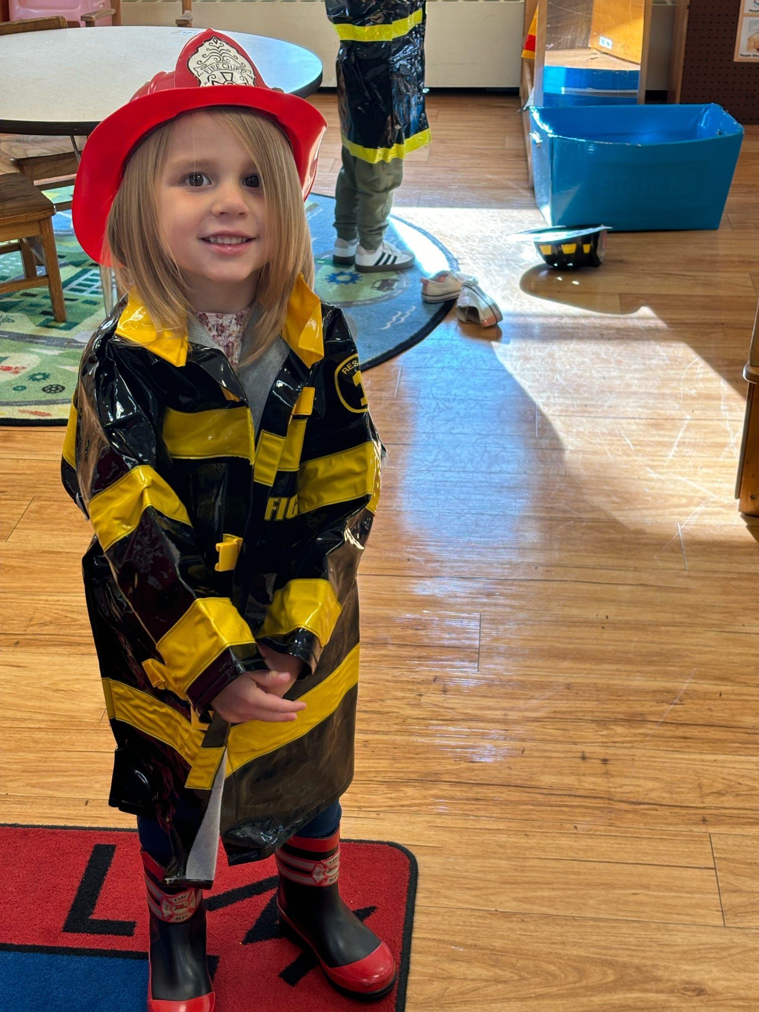 A little girl in a fireman costume is standing in a room.