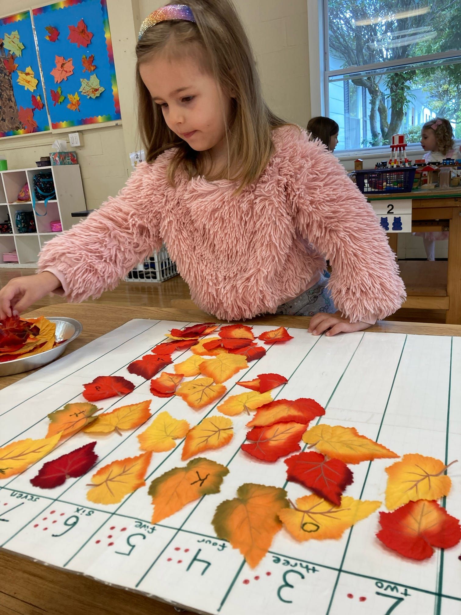 A little girl is playing with leaves on a table in a classroom.