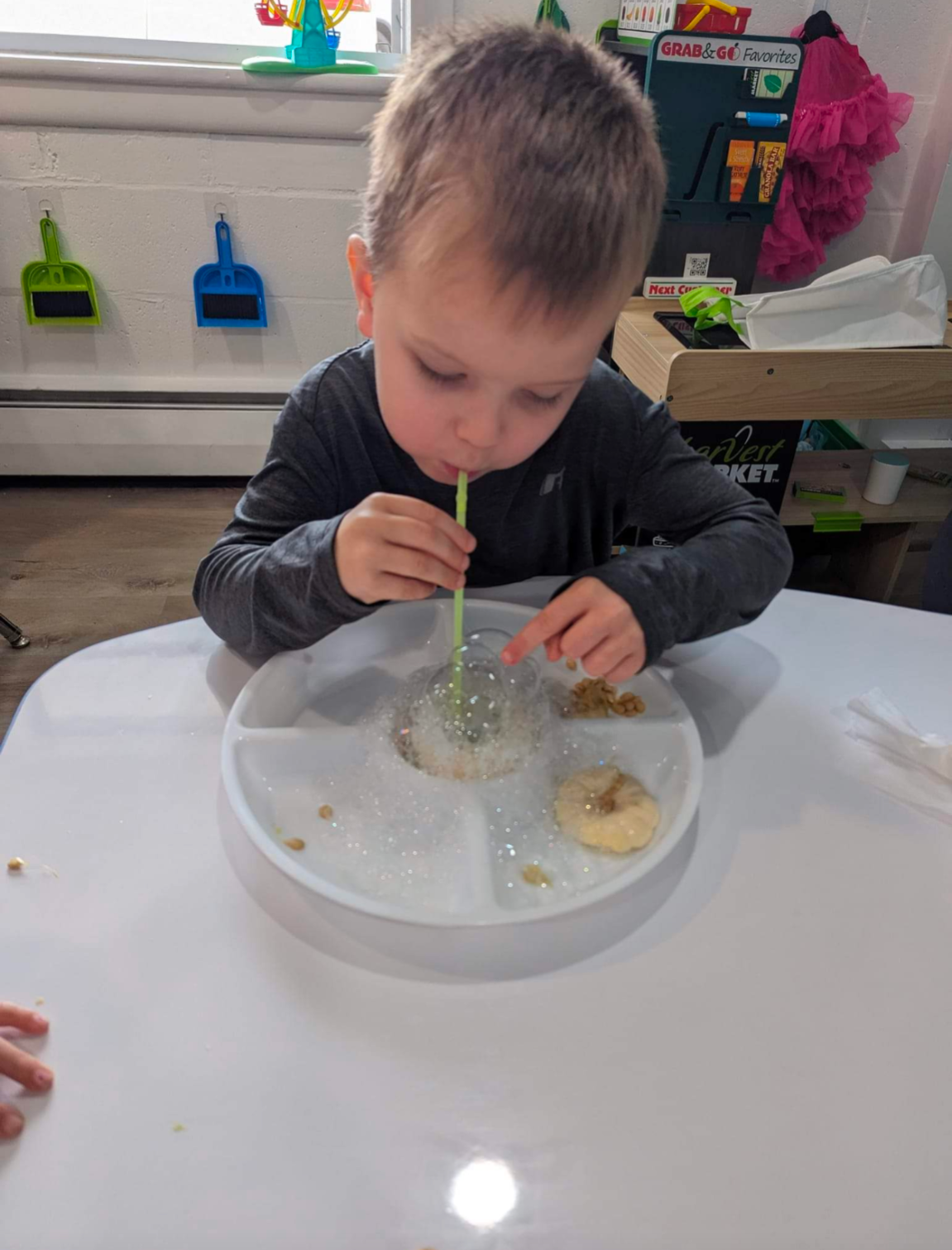 A young boy is sitting at a table eating food with a straw.