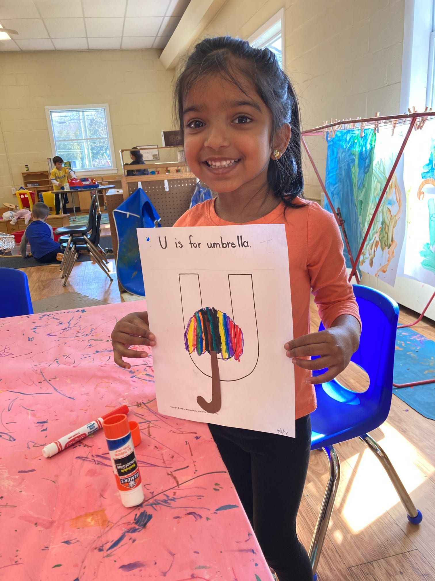 A little girl is holding a piece of paper with a drawing of an umbrella on it.