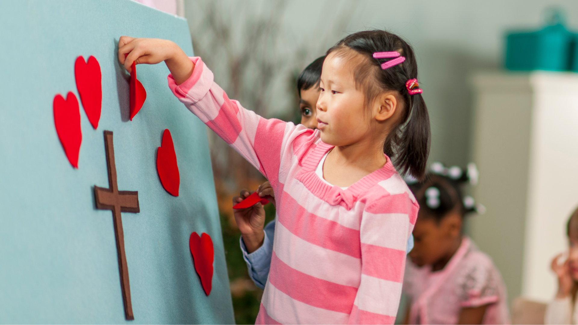 A little girl is putting hearts and a cross on a board.