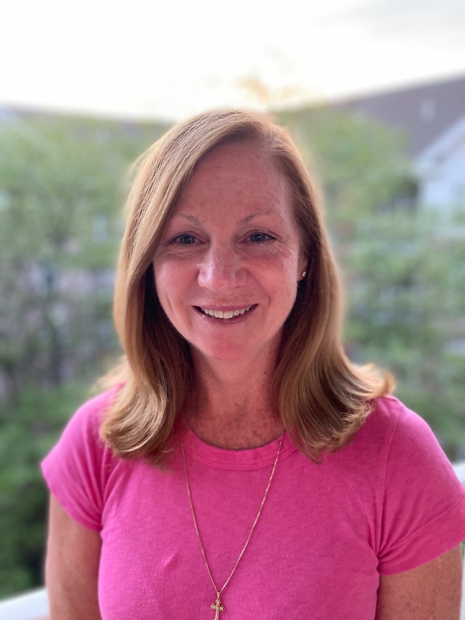 A woman in a pink shirt and necklace is smiling for the camera.