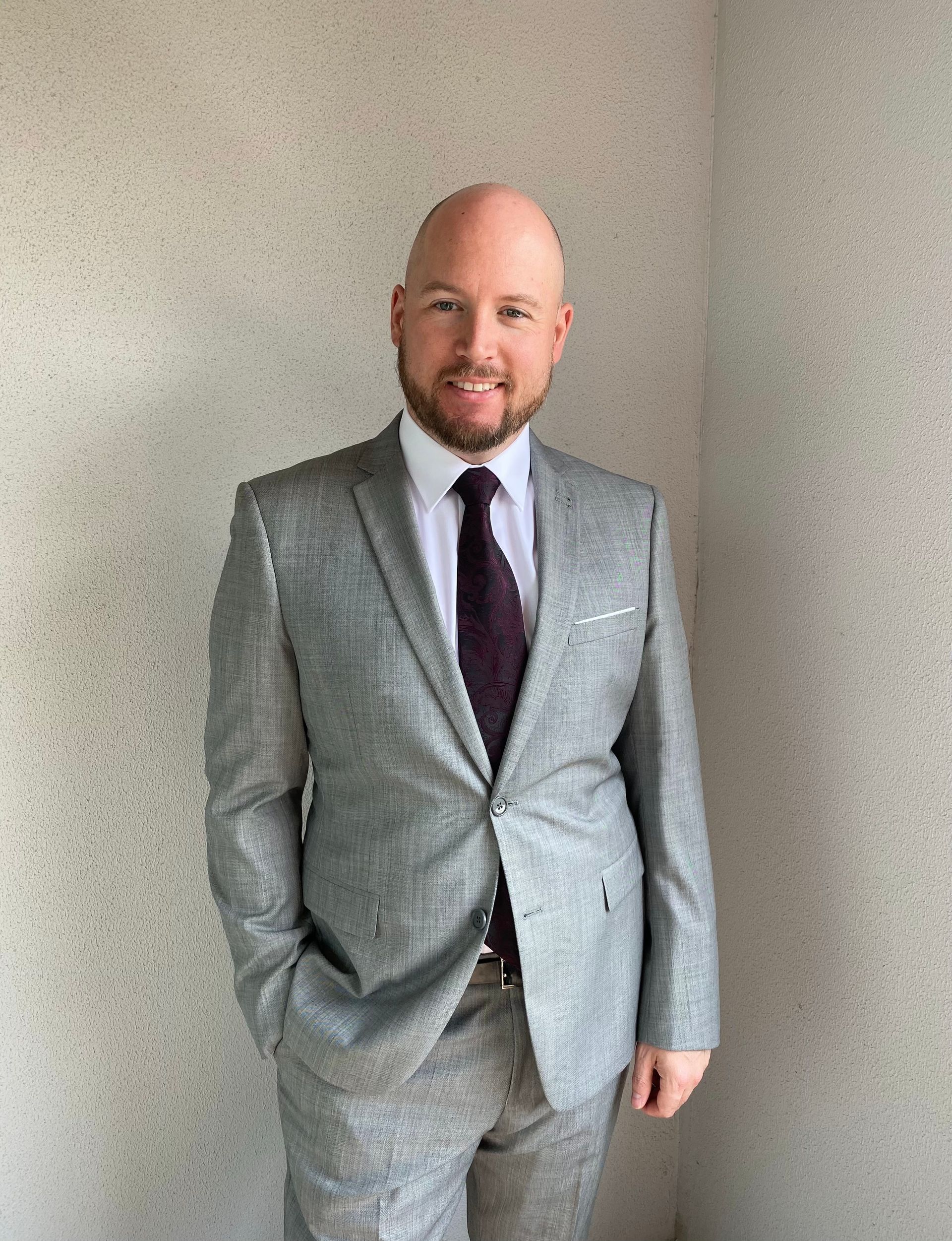Brett Peter Saunders in his gray suit and purple tie, smiling, ready to help you buy your first home!