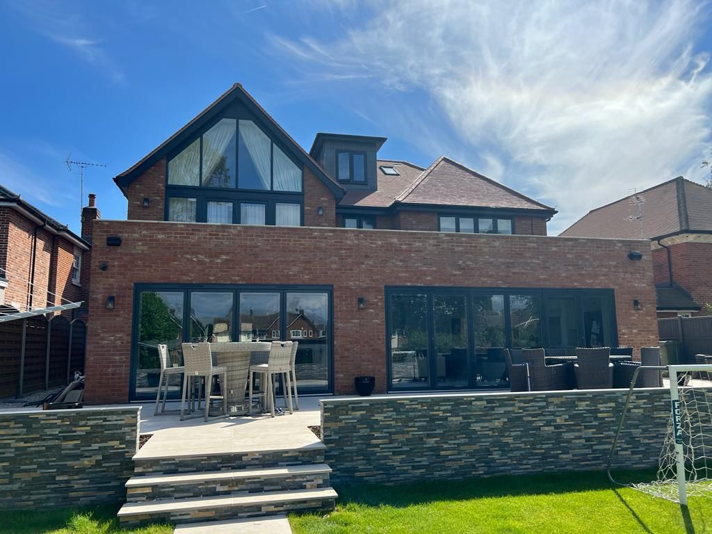 The back of a large brick house with a anthracite grey windows and bifold doors with patio table and chairs