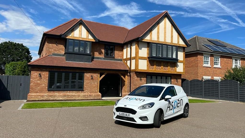 A Aspen Home Improvements car is parked in front of a large brick house.
