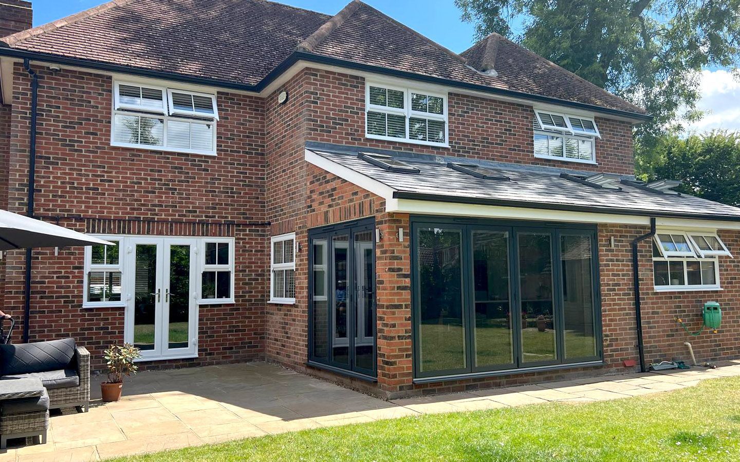 Red brick house with a glass-walled extension, white window frames, and tiled roof, on a sunny day.