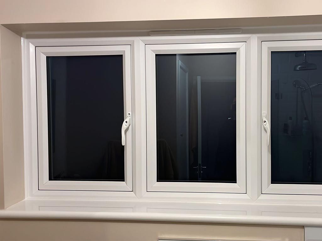 Three white windows are sitting on a window sill in a room.