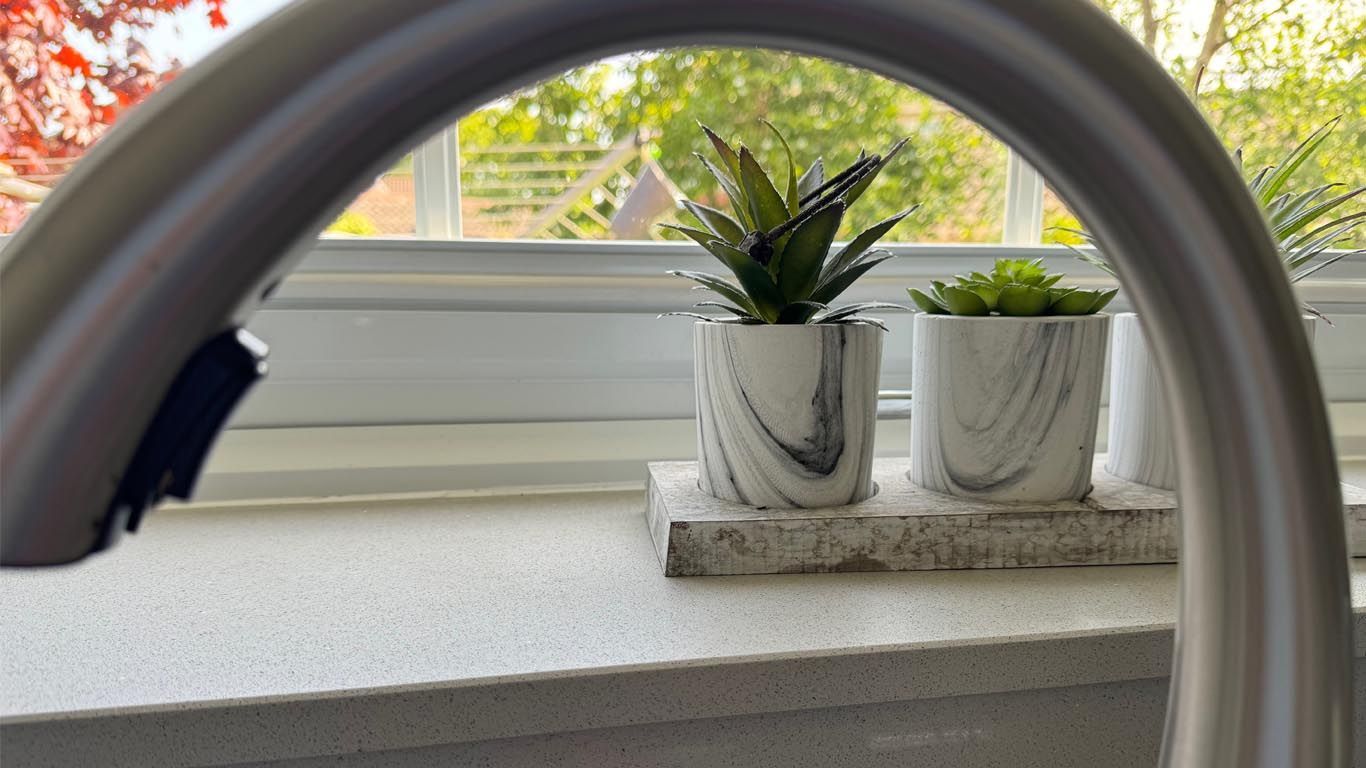 Two potted plants are sitting on a kitchen window sill with tap

