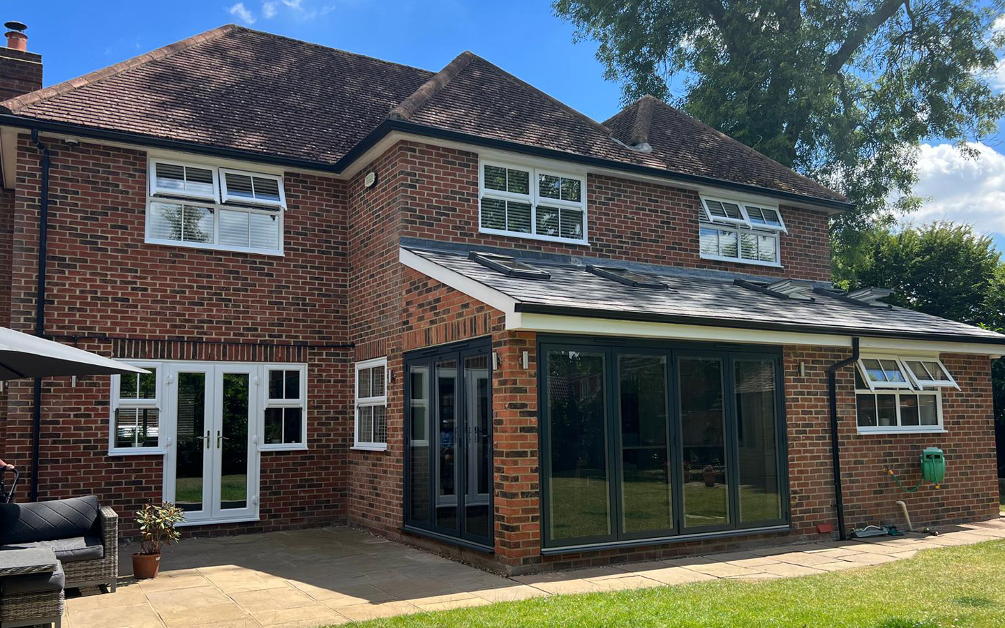 Brick house with white windows, glass doors, and a tiled roof, sunny day.