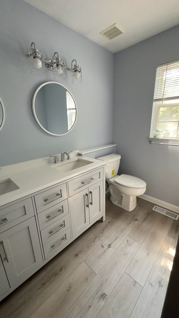 A bathroom with a sink , toilet , mirror and window.