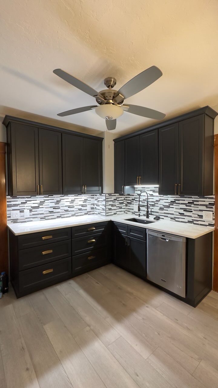 A kitchen with black cabinets and a ceiling fan.