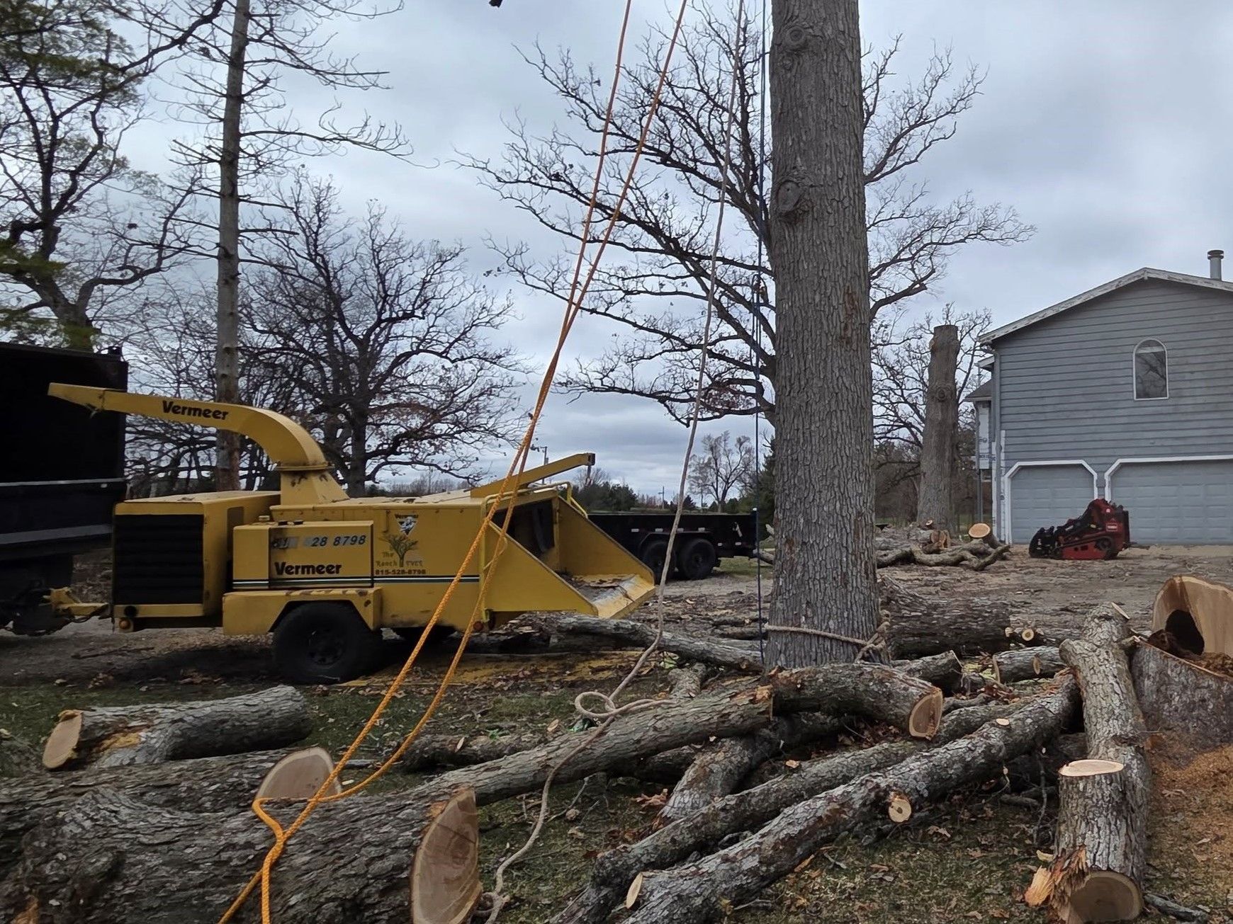 A tree chipper is cutting down a tree in front of a house. A tree chipper is cutting down a tree in front of a house.