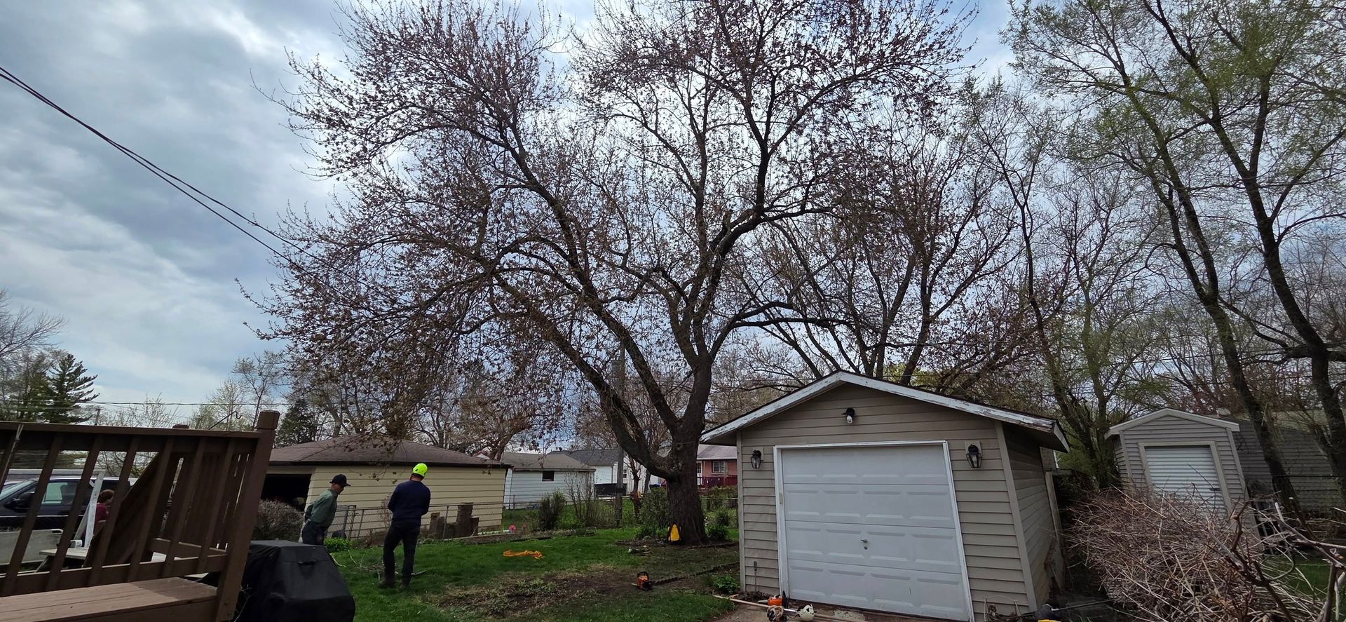 A man is standing in front of a garage with a tree in the background.
