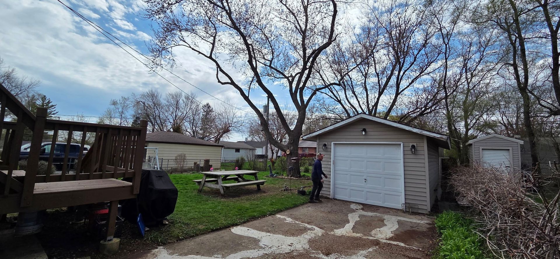 A man is standing in front of a garage with a picnic table in the backyard.