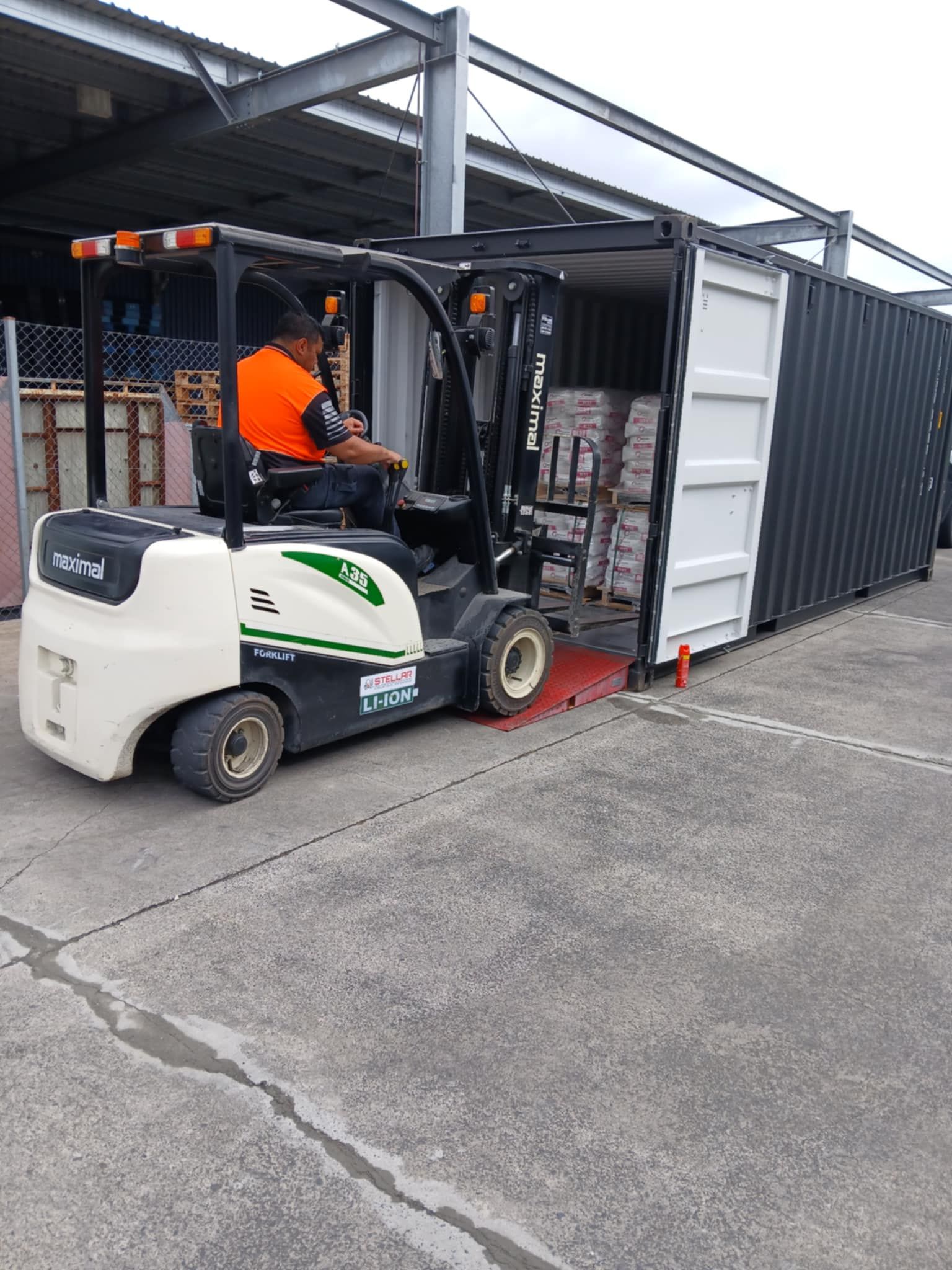 A man is driving a forklift next to a shipping container.