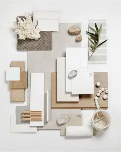 A minimalist interior design mood board featuring neutral samples, textured fabrics, stones, a shell, and a leafy sprig.