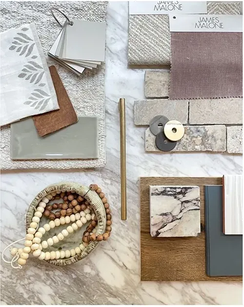 A flat-lay interior design mood board featuring marble, brick, fabric swatches, wood beads, and neutral-toned material.