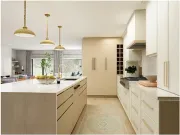 Modern kitchen with light wood cabinetry, white countertops, three pendant lights, and an island facing a living area.