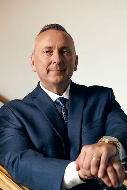 A man in a suit and tie is sitting in a chair with his hands folded.