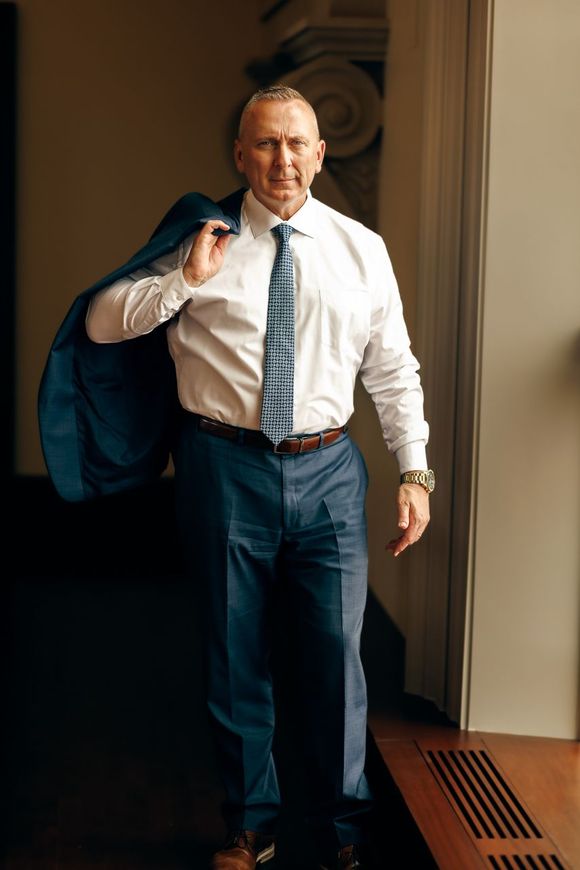 A man in a suit and tie is holding a jacket over his shoulder.