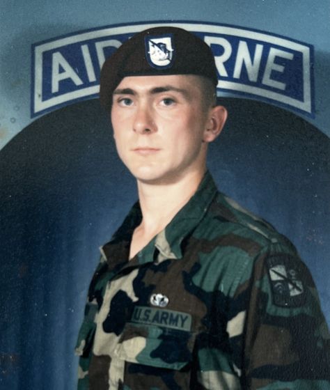 A man in a us army uniform stands in front of an airborne sign