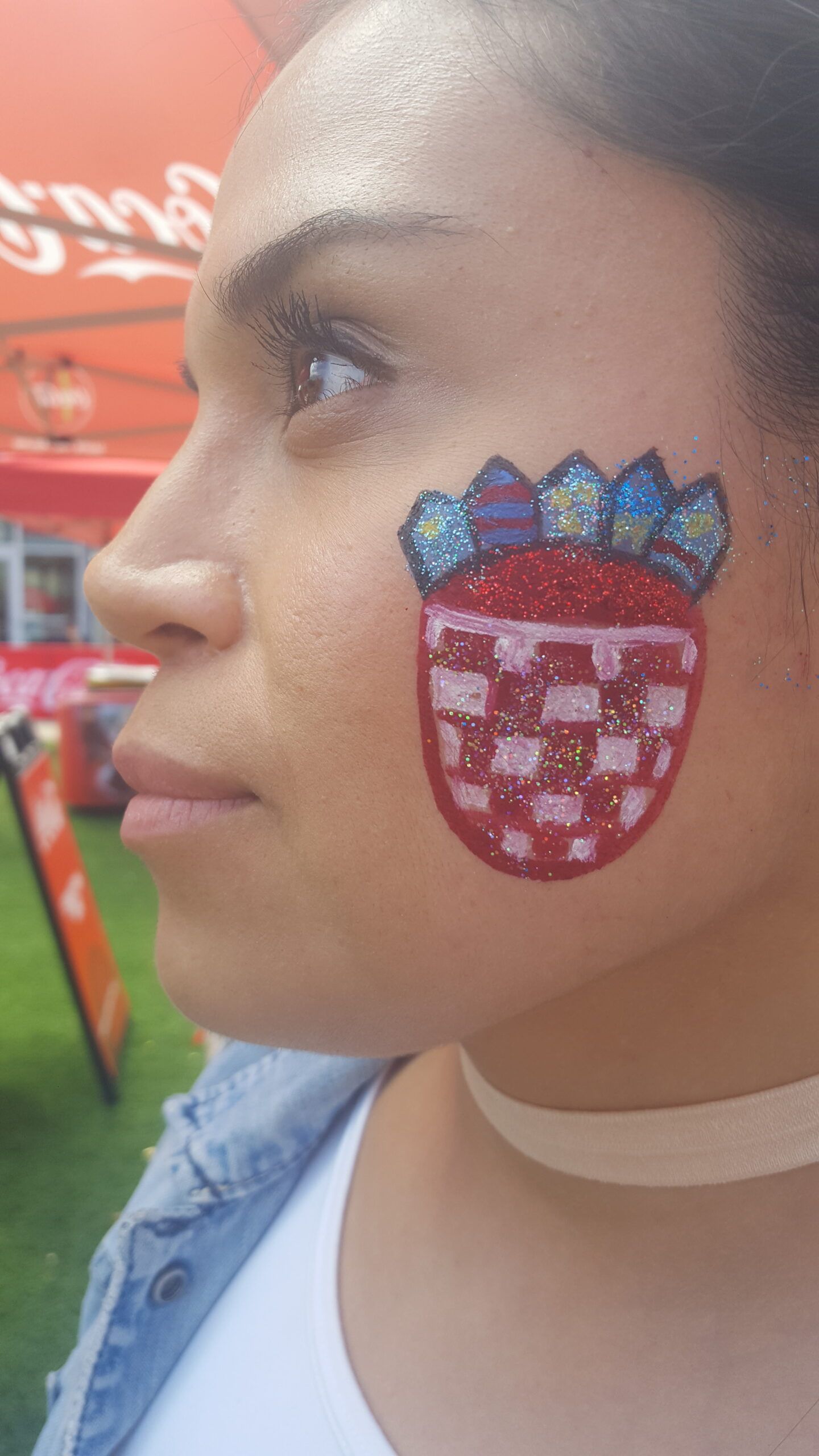 A woman has a strawberry painted on her face.