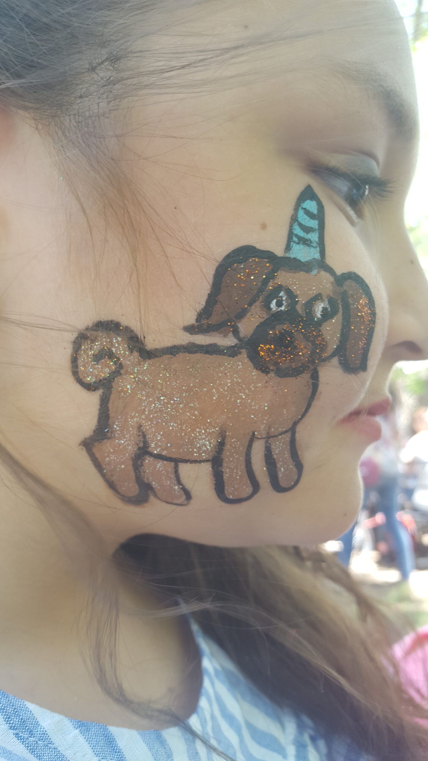 A little girl has a pug dog with a unicorn horn painted on her face.