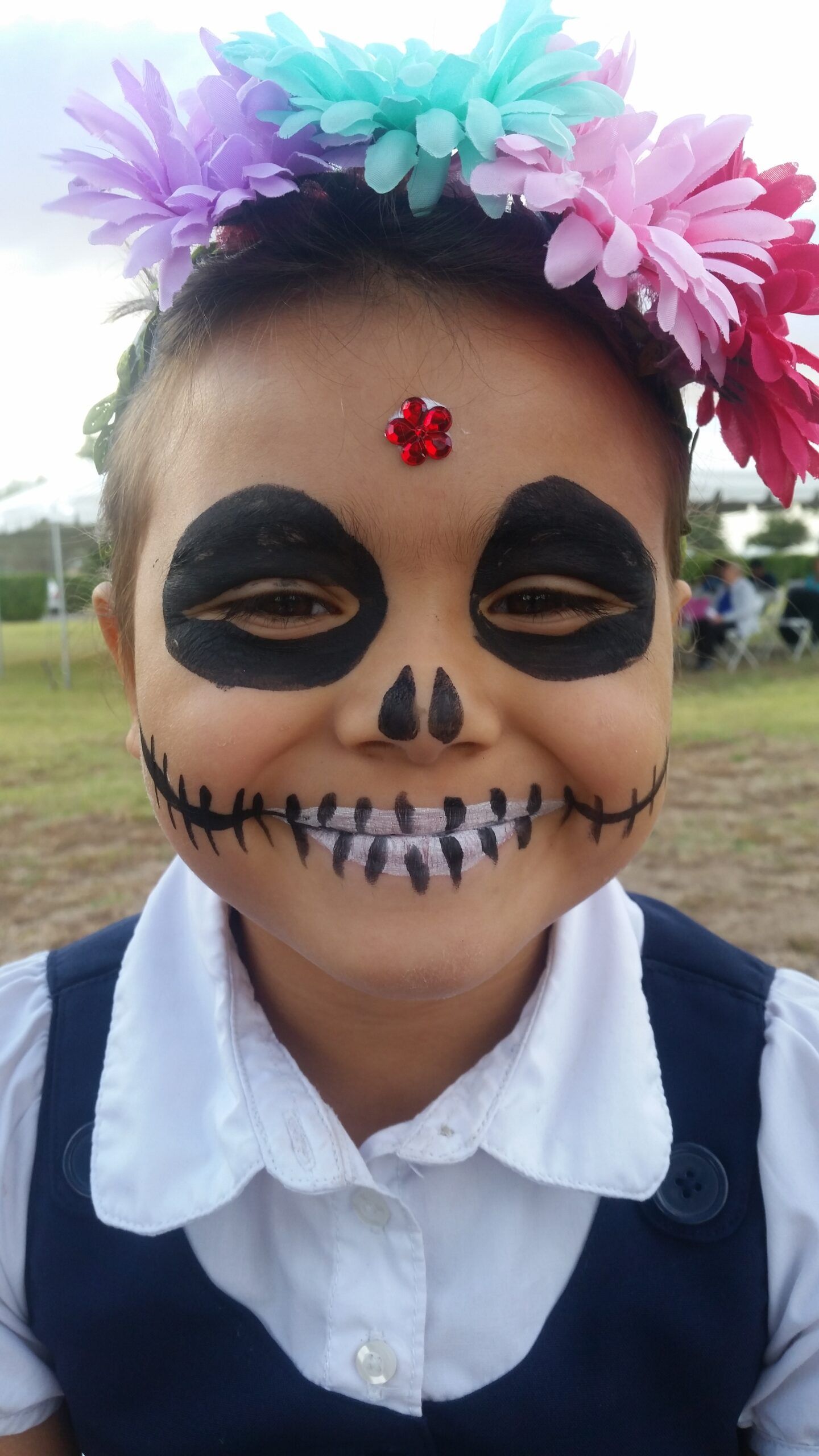 A little girl with her face painted like a skull and flowers in her hair.