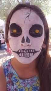 A little girl with her face painted like a skeleton.