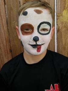 A young boy with his face painted like a dog with his tongue sticking out.