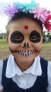 A little girl has her face painted like a skeleton and has flowers in her hair.