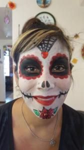 A woman with sugar skull makeup on her face is smiling.