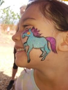 A little girl has a blue unicorn painted on her face.