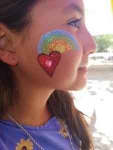 A little girl has a rainbow and a heart painted on her face.