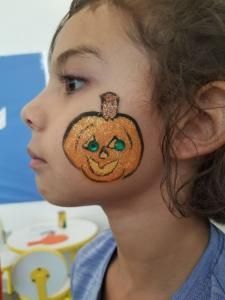 A little girl has a pumpkin painted on her face.
