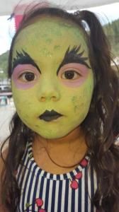 A little girl with her face painted like the witch from the wizard of oz.