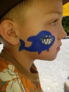 A young boy has a blue shark painted on his face